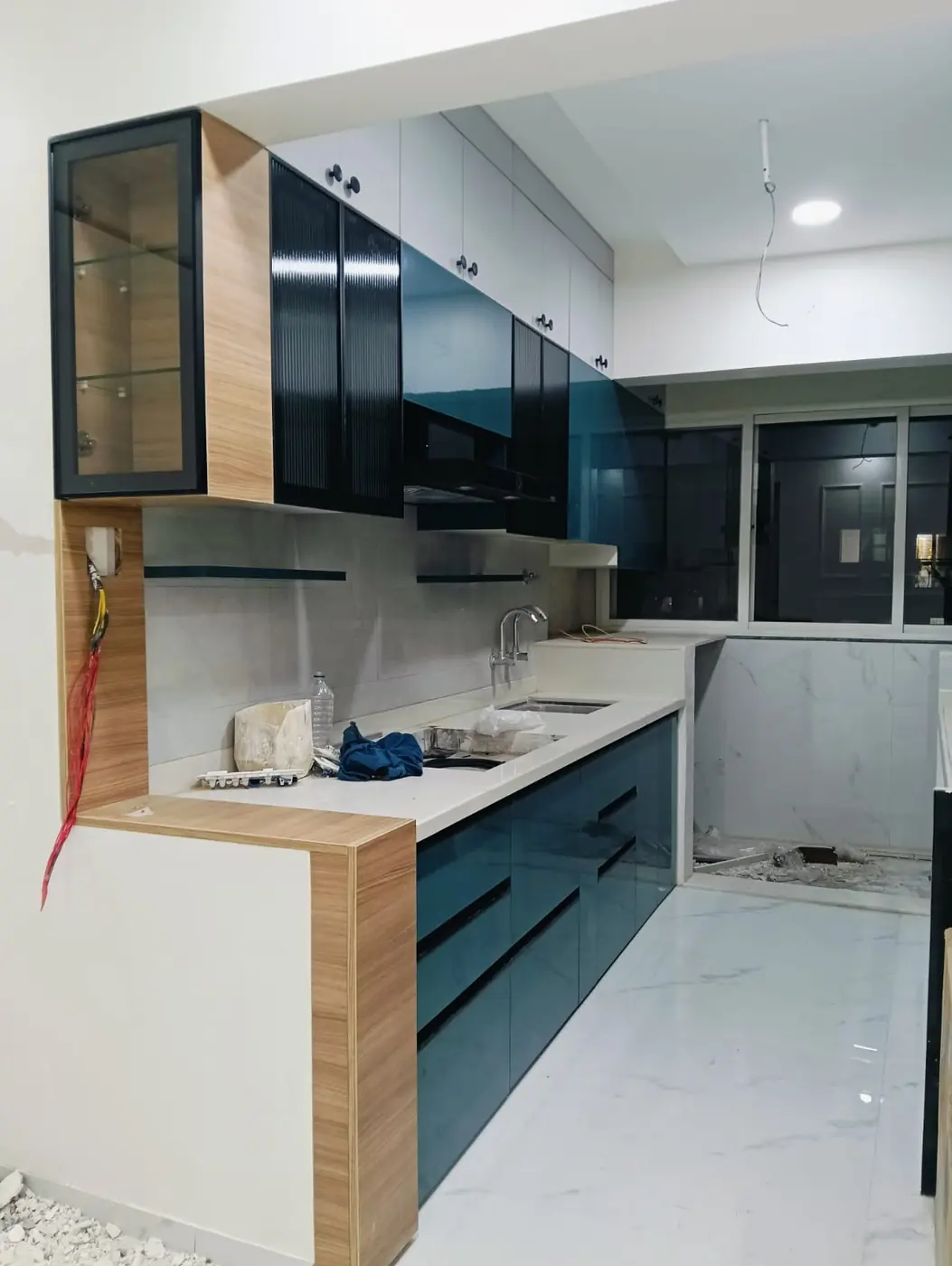 Teal acrylic modular kitchen with wooden end panel and glass wall unit, Pune